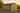 Wooden shed with a black roof in a rural setting during sunset.